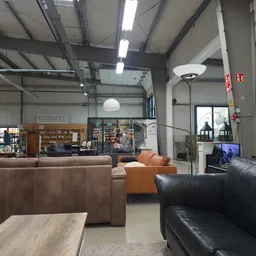 Winkelvloer met bruine en zwarte leren zitmeubels, houten tafel, stellingen met spullen en winkelafdelingen op de achtergrond