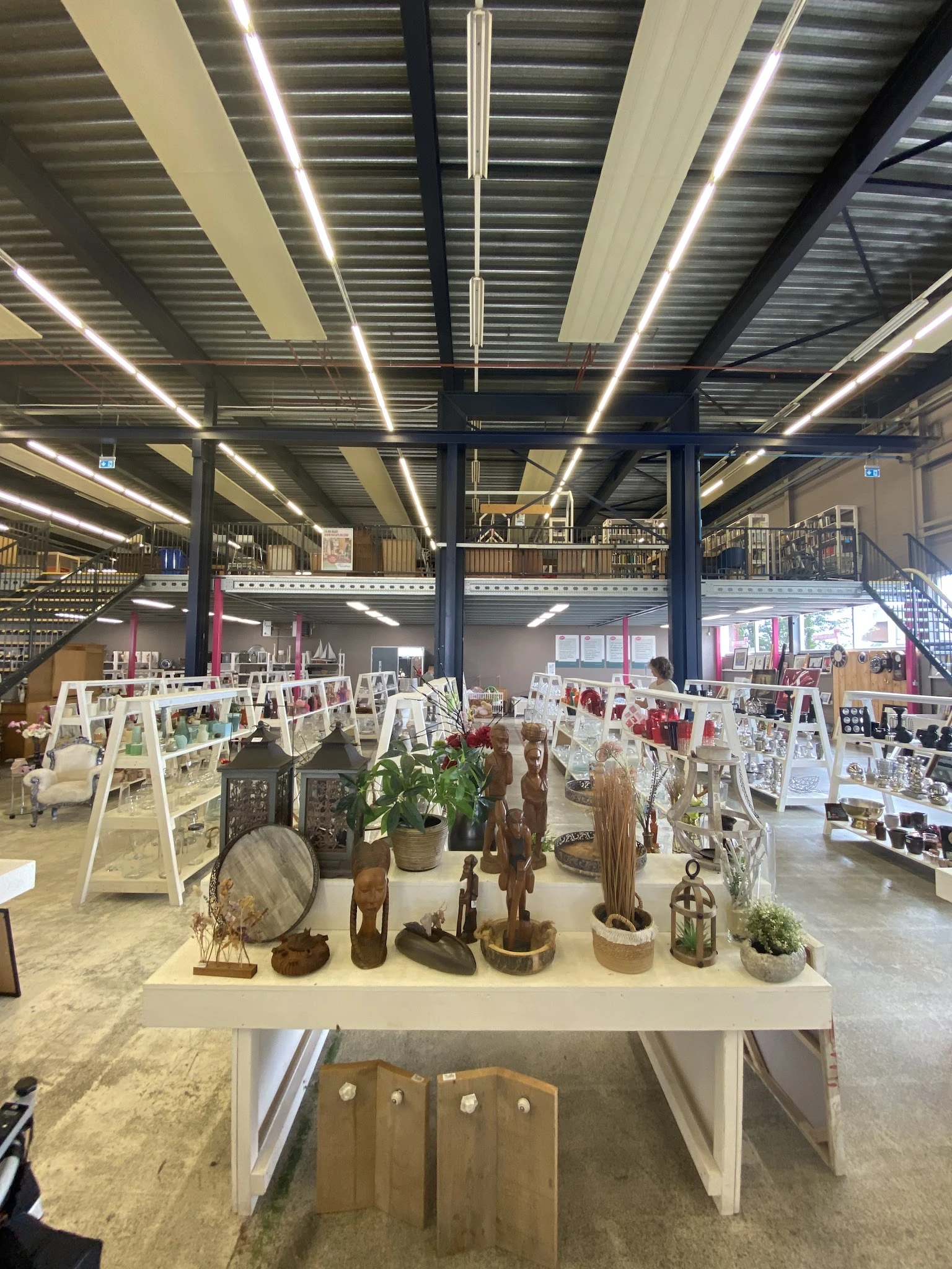 Kringloopwinkel met houten kunstobjecten, plantenbakken en schilderijen op ezel-tentoonstellingen op de vloer, stellingen met