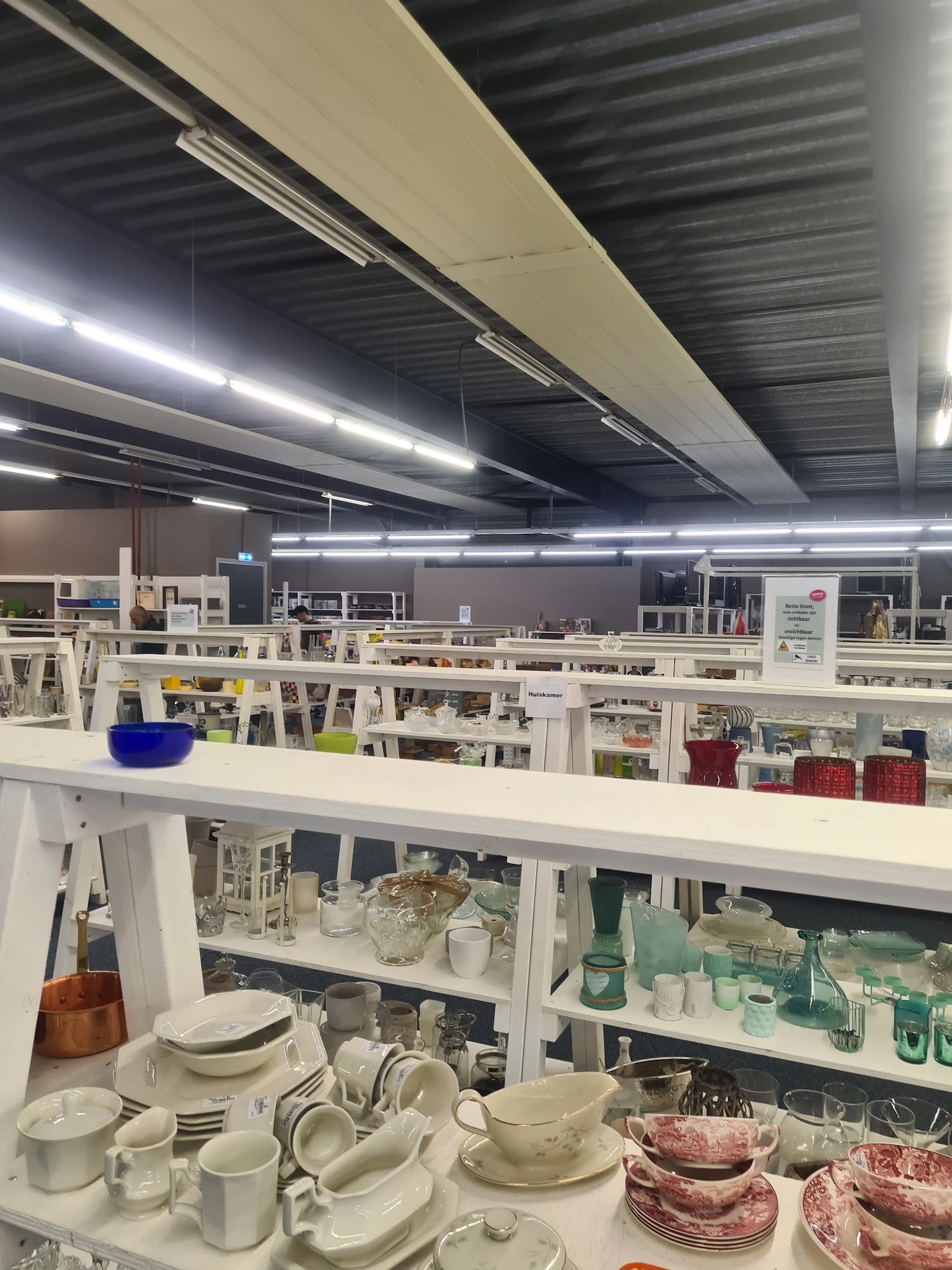 Winkelvloer met witte stellingen en rekken vol huishoudartikelen en decoratieve spullen onder LED-verlichting