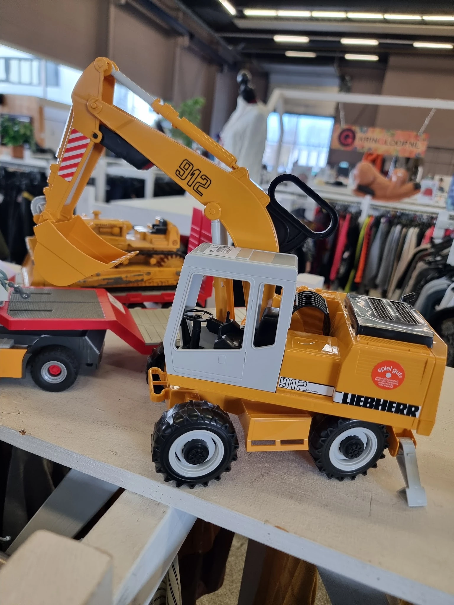 Gele Liebherr speelgoedgraafmachine met witte cabine en zwarte wielen op houten display