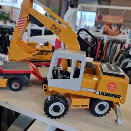 Gele Liebherr speelgoedgraafmachine met witte cabine en zwarte wielen op houten display