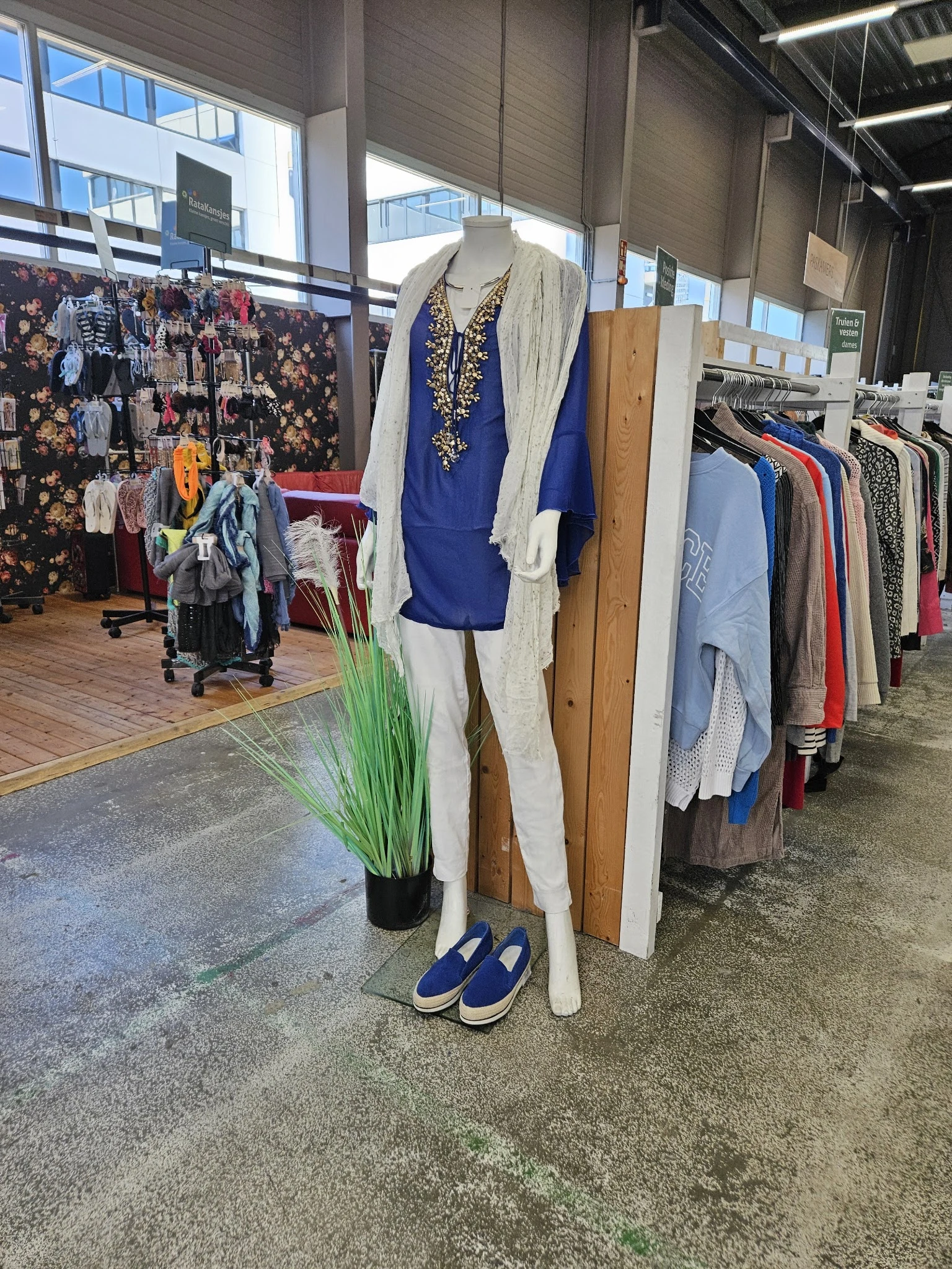 Rekken met tweedehands kleding en een display met blauwe jurk en witte cardigan