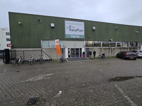 Voorkant van kringloopwinkel RataPlan met groene golfplaten gevel, ingang met glazen deuren en fietsen geparkeerd ervoor