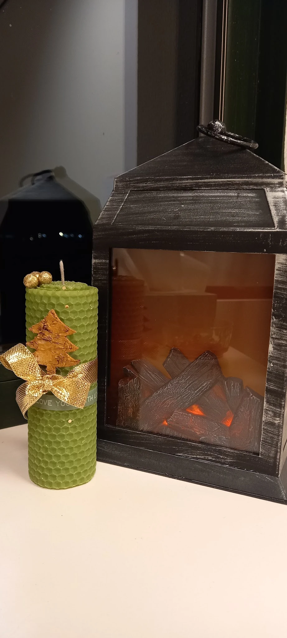 Groene decoratieve kaars met gouden kerstboom en ster, naast bruine houtkachel