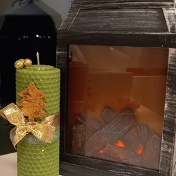 Groene decoratieve kaars met gouden kerstboom en ster, naast bruine houtkachel