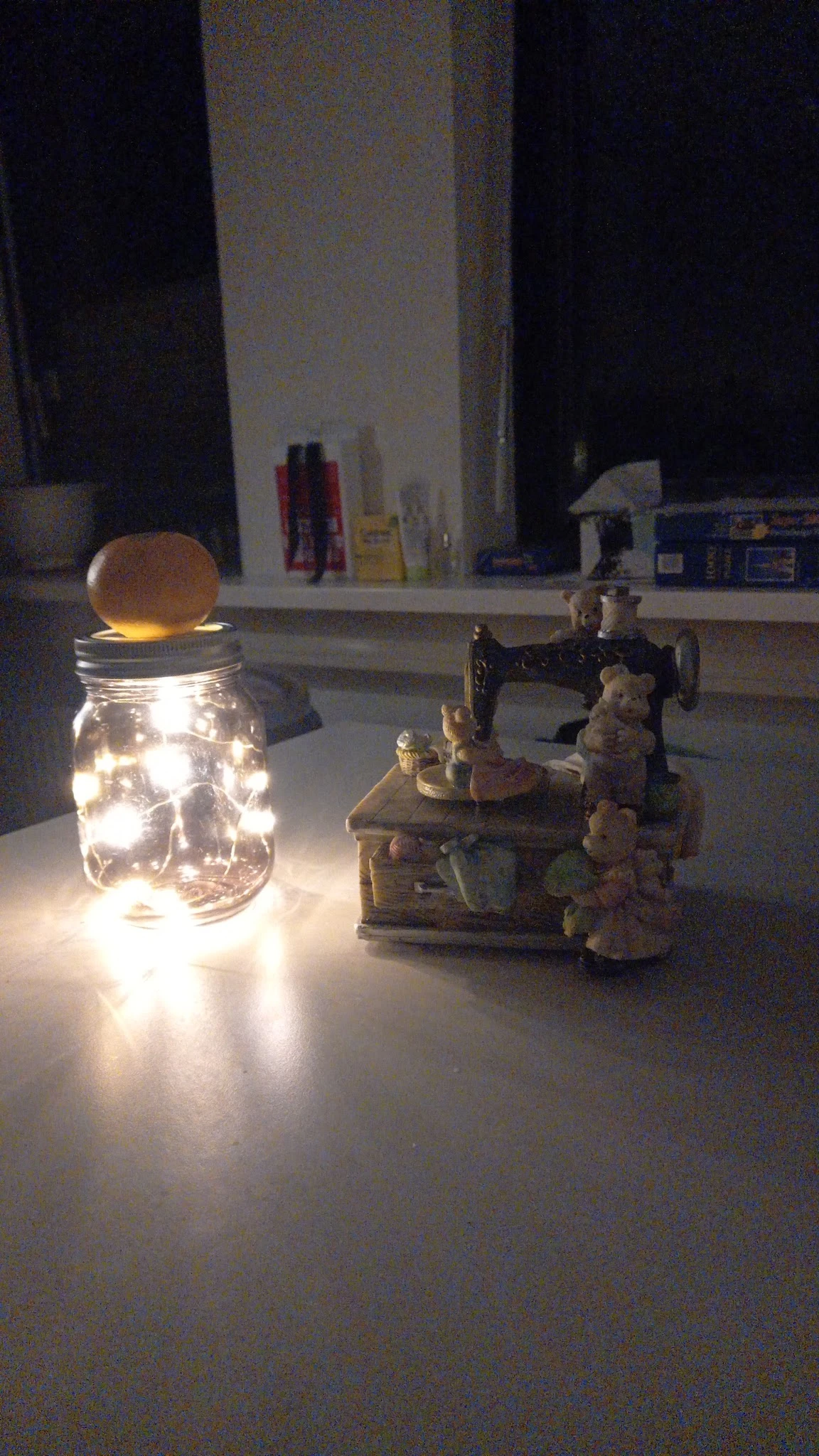 Glazen pot met warm licht en houten deksel, naast een vintage naaitmachine met decoratieve figuren
