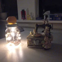 Glazen pot met warm licht en houten deksel, naast een vintage naaitmachine met decoratieve figuren