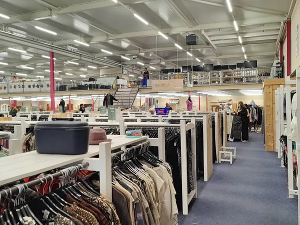 Overzicht van de winkelvloer met kledingrekken, tafels met spullen en bezoekers in een grote hal