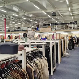 Overzicht van de winkelvloer met kledingrekken, tafels met spullen en bezoekers in een grote hal