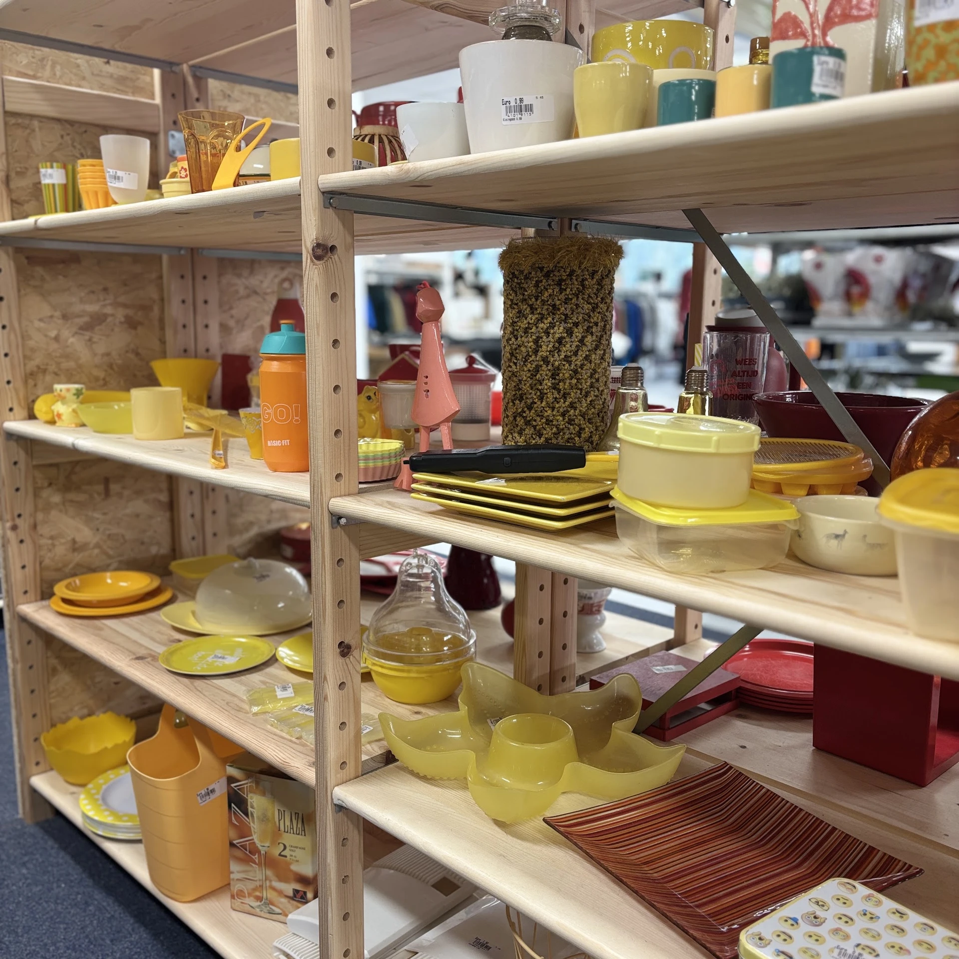 Stellingkast met geel serviesgoed, pannen, glazen fles en huishoudelijke spullen in een kringloopwinkel