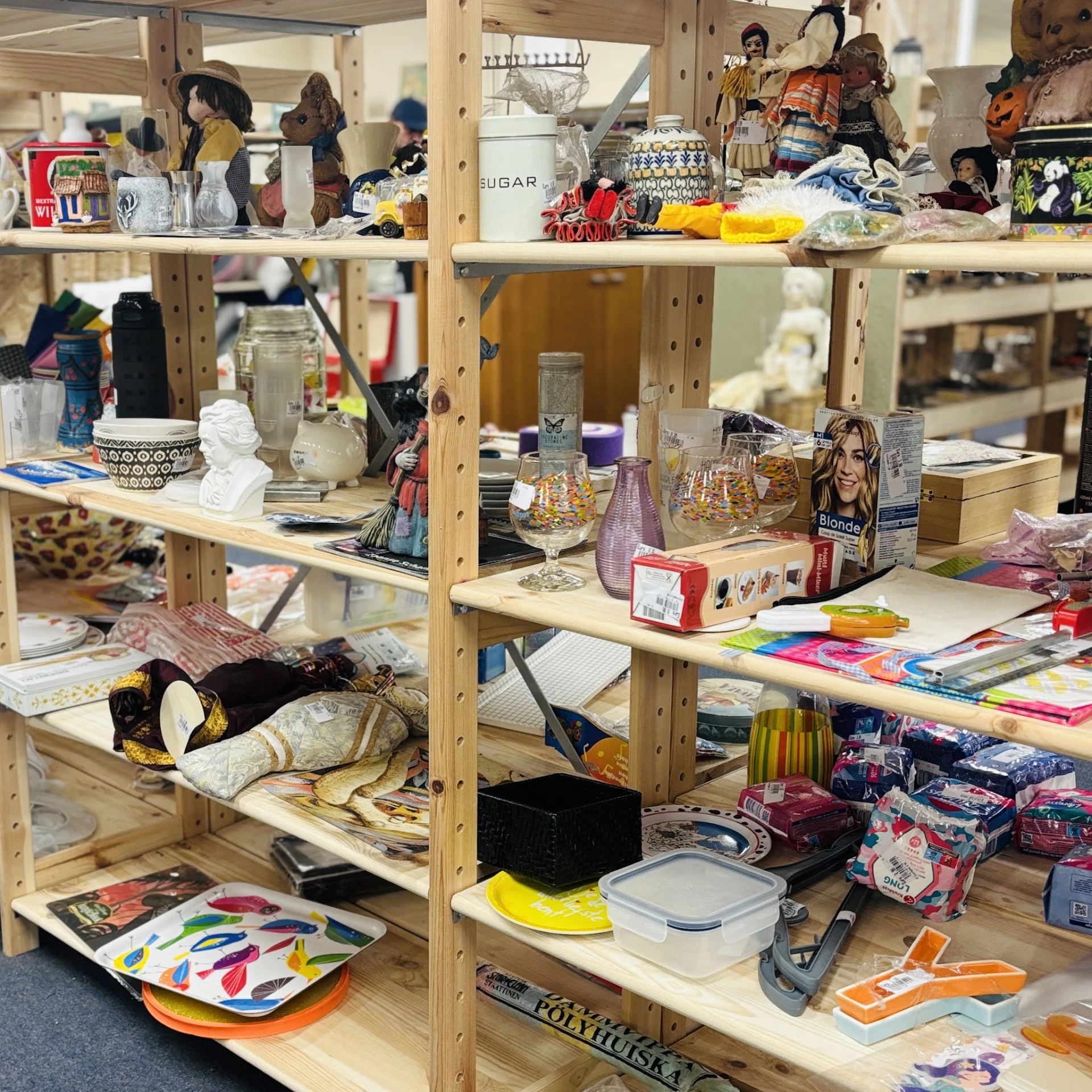 Houten stellingen gevuld met diverse tweedehands spullen, decoraties, boeken en huishoudartikelen in een kringloopwinkel