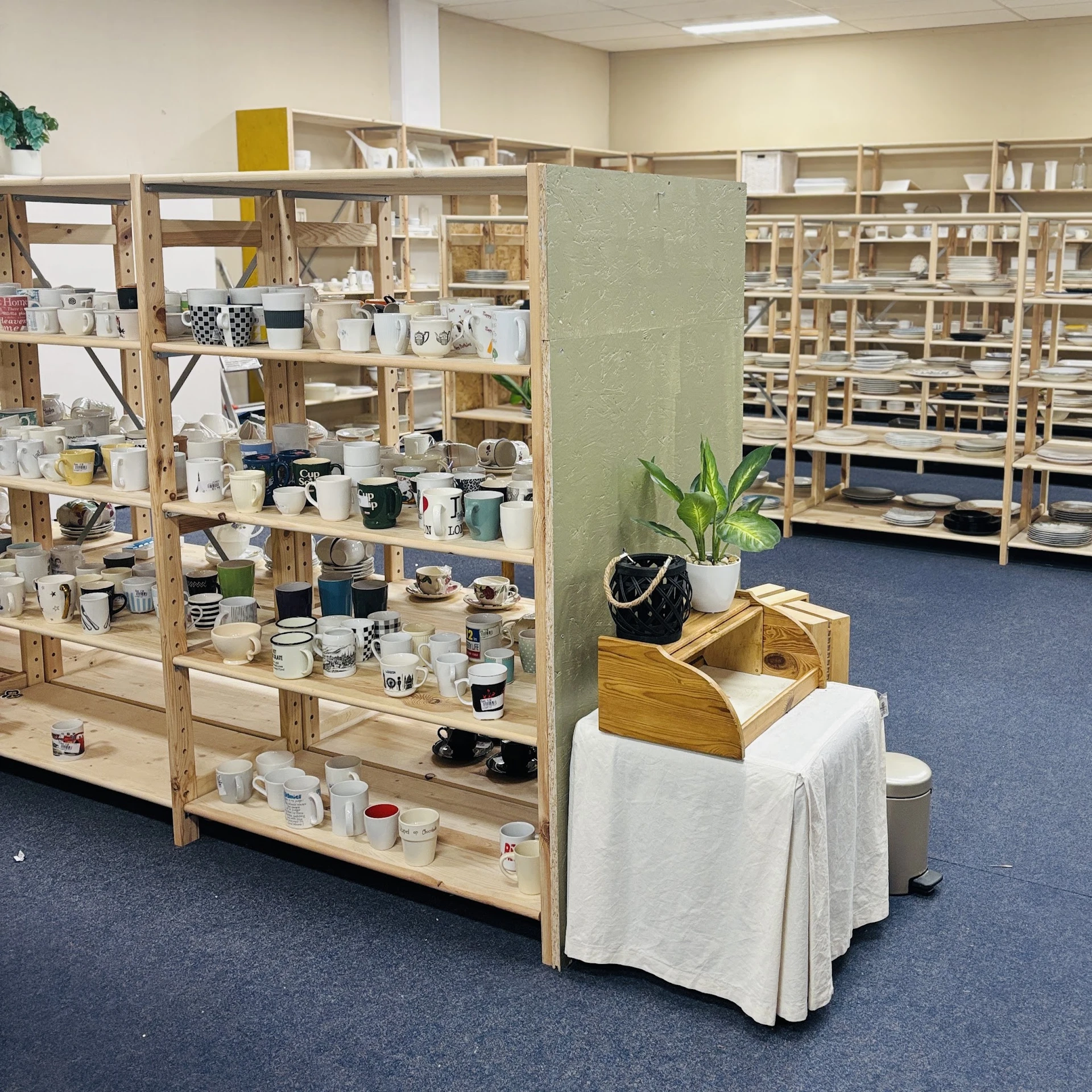 Houten stellingen vol huishoudartikelen, servies en decoratie in een kringloopwinkel