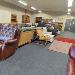 Winkelvloer met diverse meubels: bruine leren fauteuils, gele stoelen, kasten en opstellingen in kringloopwinkel