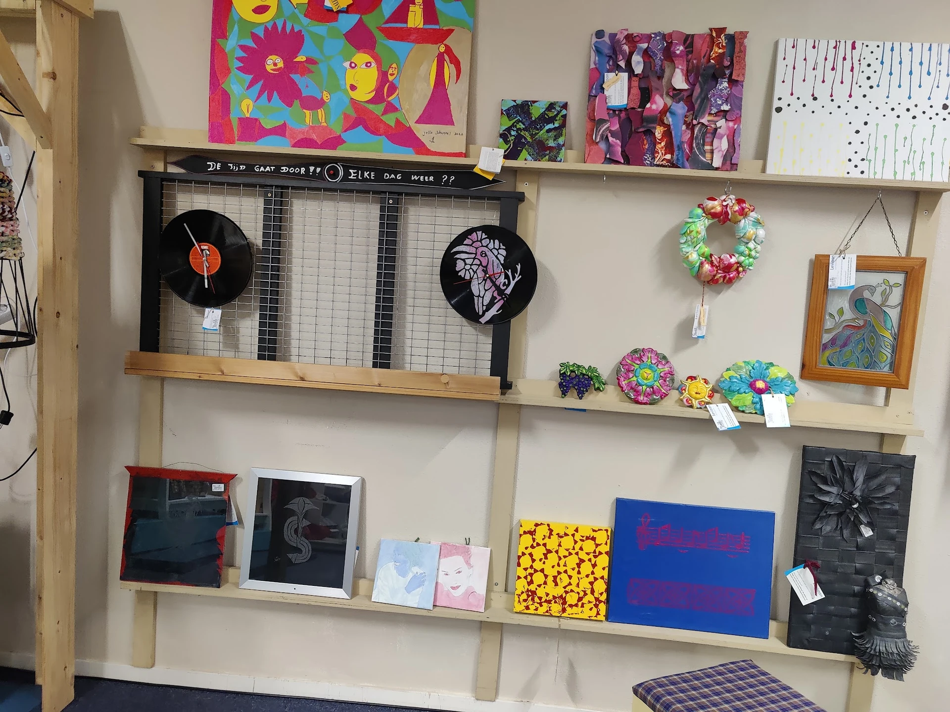 Houten wandplanken met uitgestalde tweedehands kunst, decoratie en vintage items zoals vinyl records, schilderijen en handgem