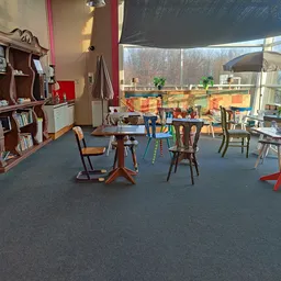 Speelruimte met tafels, stoelen en speelgoed bij ramen met uitzicht op speeltuin