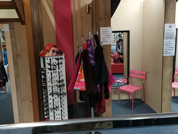 Winkelinterieur met kledingrekken, uitgestalde kleding, roze stoelen en houten palen