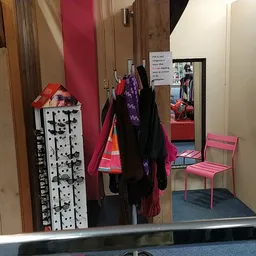 Winkelinterieur met kledingrekken, uitgestalde kleding, roze stoelen en houten palen
