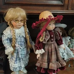 Vier porseleinpoppen met vintage kleding en accessoires in een houten kast