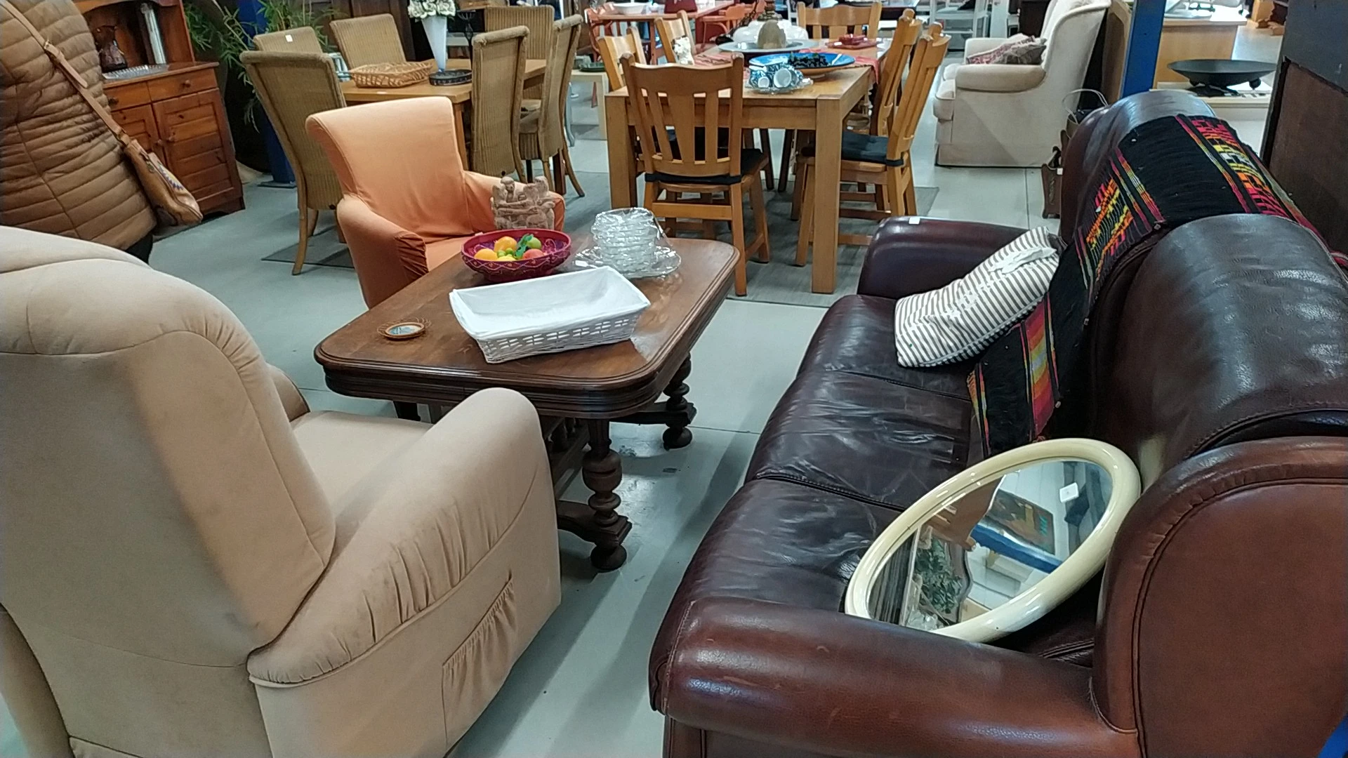 Winkelvloer met diverse meubels: een houten tafel met stoelen, fauteuils in beige en zwart leer, en andere zitmeubels in de k