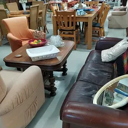 Winkelvloer met diverse meubels: een houten tafel met stoelen, fauteuils in beige en zwart leer, en andere zitmeubels in de k