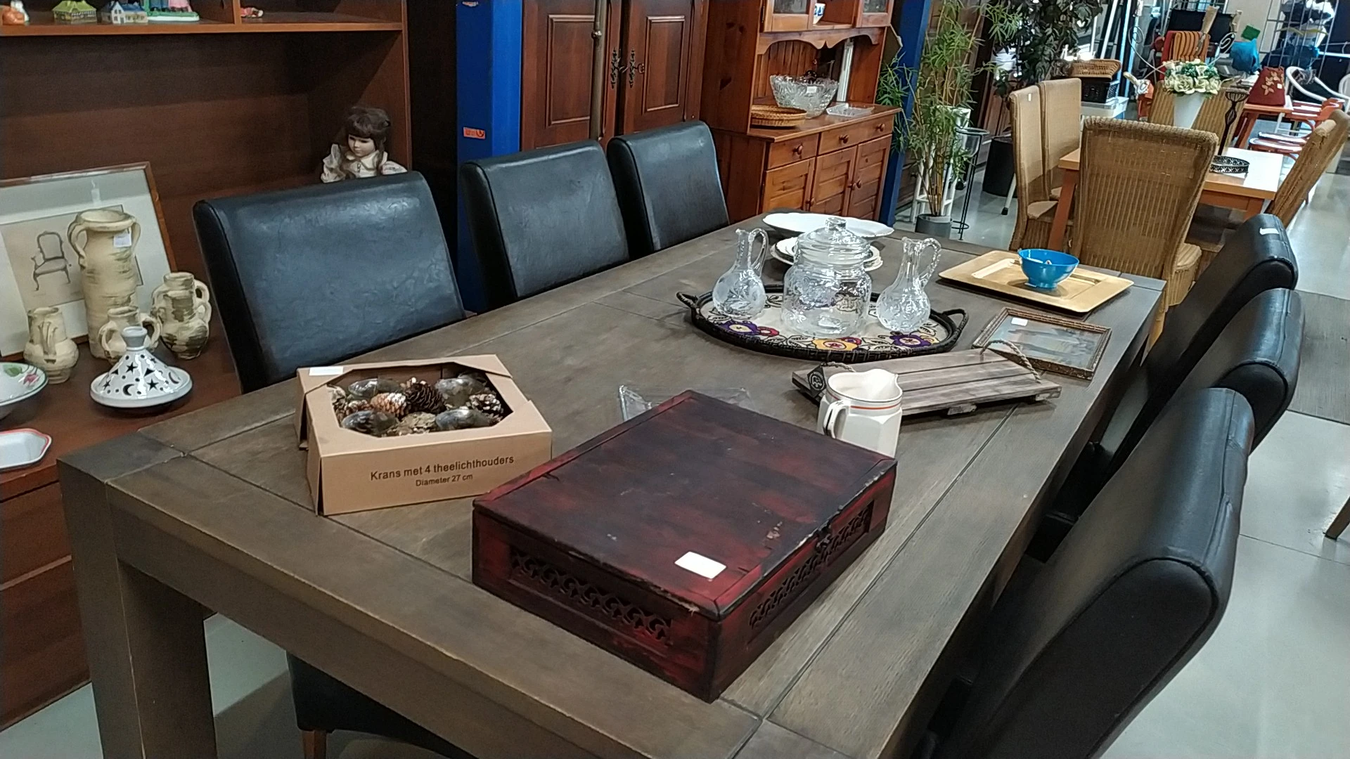 Grijze eettafel met blauwe stoelen, decoratieve items en dozen in een ingerichte kringloopwinkel