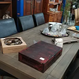 Grijze eettafel met blauwe stoelen, decoratieve items en dozen in een ingerichte kringloopwinkel