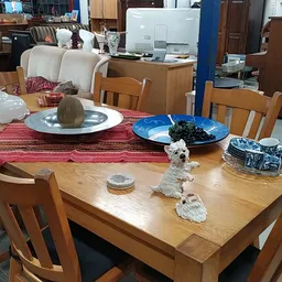 Houten eettafel met stoelen, rode tafelloper en diverse voorwerpen in een kringloopwinkel
