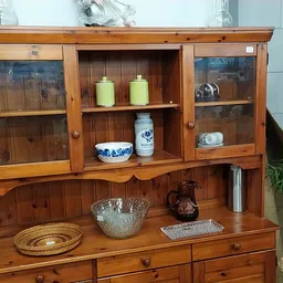 Houten vitrinekast met gesloten kastjes en glazen deuren, gevuld met decoratieve objecten en serviesgoed