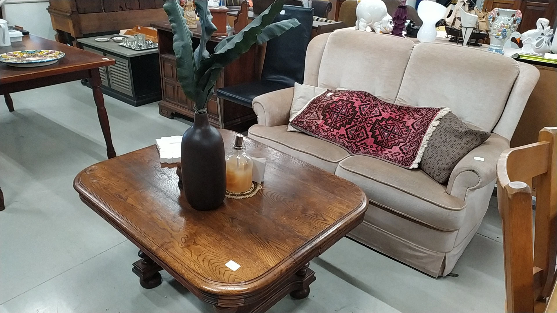 Houten salontafel met decoratieve zwarte vaas en bloemen, naast beige sofa met kussens in thuisinrichting