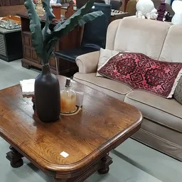 Houten salontafel met decoratieve zwarte vaas en bloemen, naast beige sofa met kussens in thuisinrichting