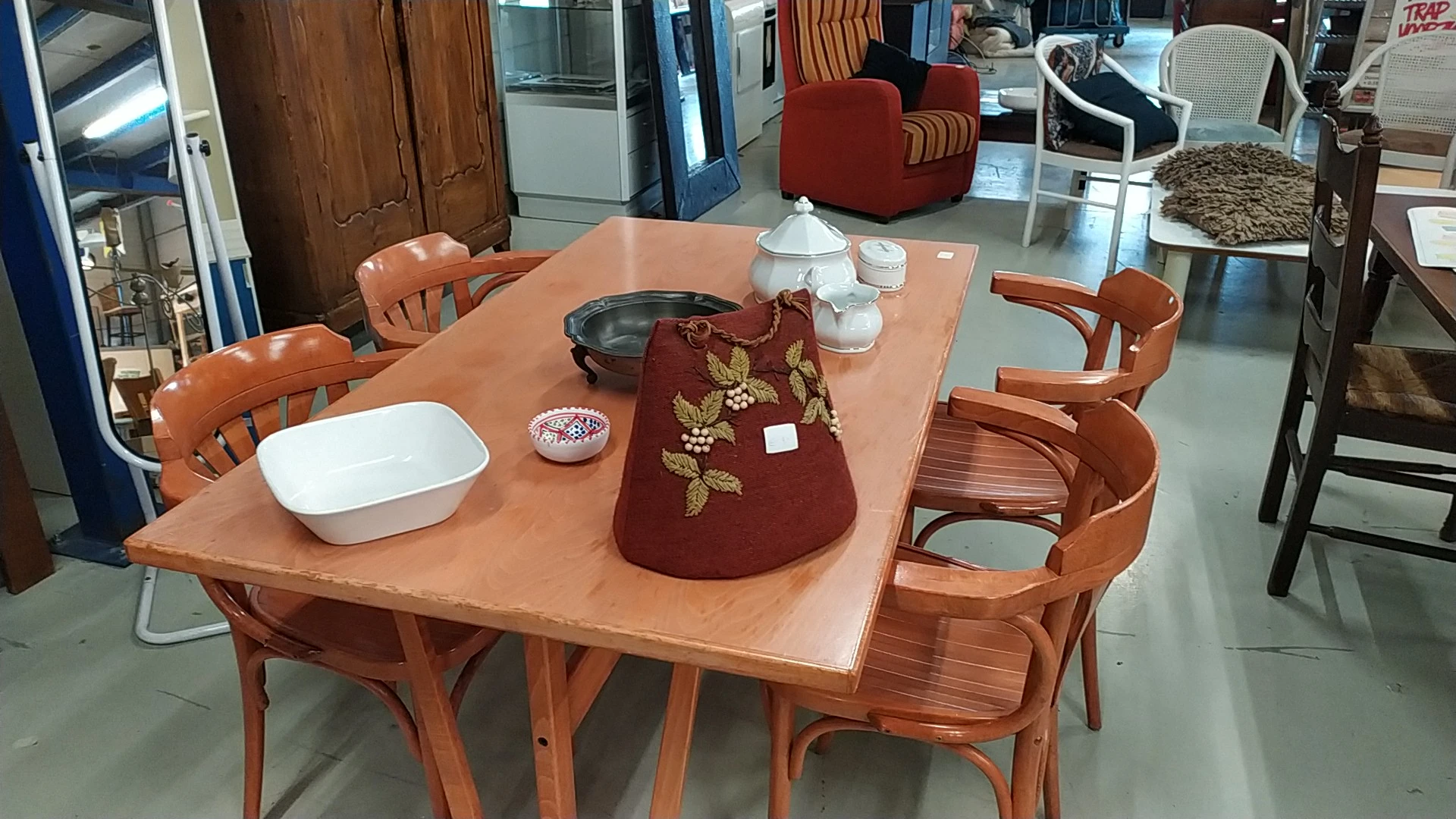 Houten eettafel met stoelen, gedekt met servies, pannen en een rood borduurwerk kussen