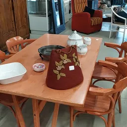 Houten eettafel met stoelen, gedekt met servies, pannen en een rood borduurwerk kussen