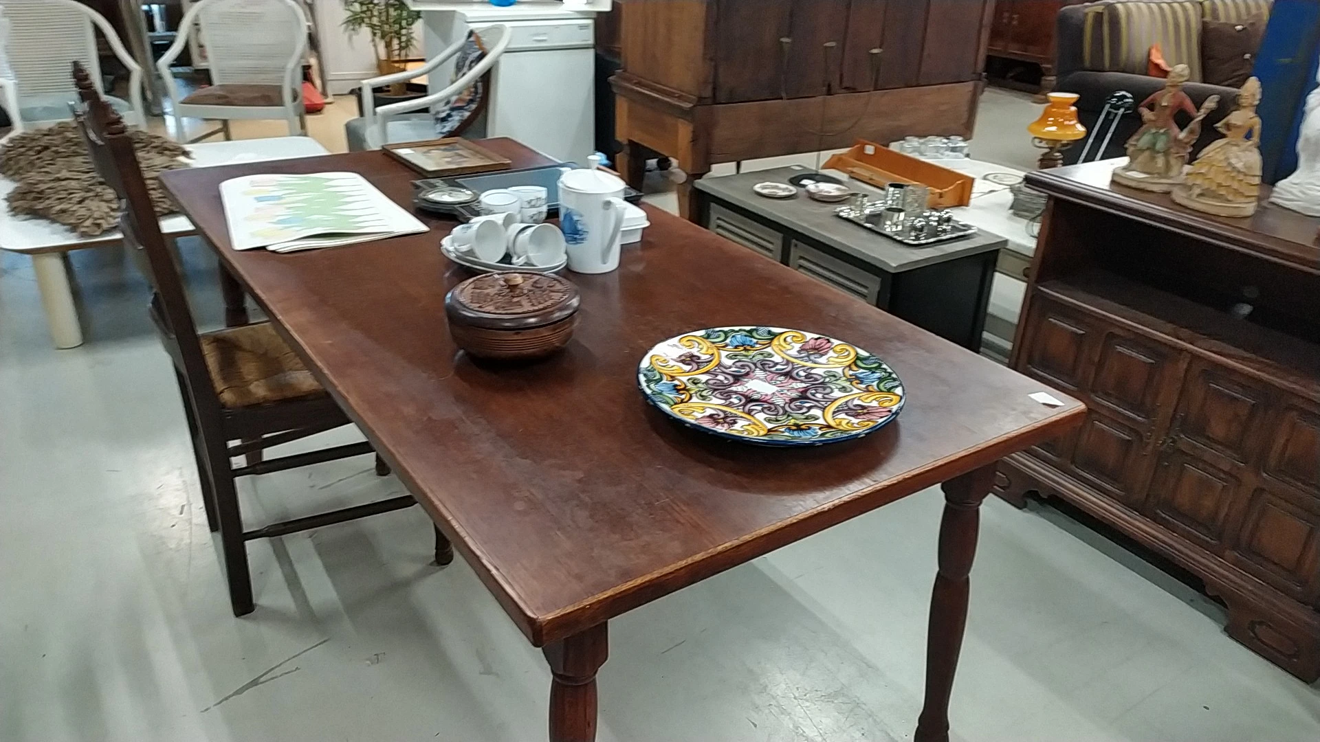 Houten eettafel met decoratieve borden en huishoudartikelen in een kringloopwinkel