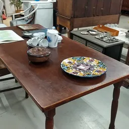 Houten eettafel met decoratieve borden en huishoudartikelen in een kringloopwinkel