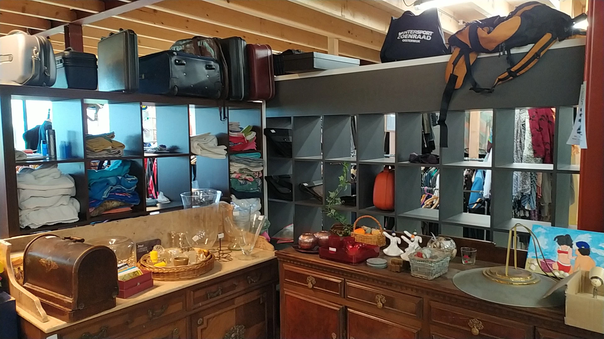 Kringloopwinkelinterieur met stellingen vol tweedehands spullen, houten kasten met servies en decoraties