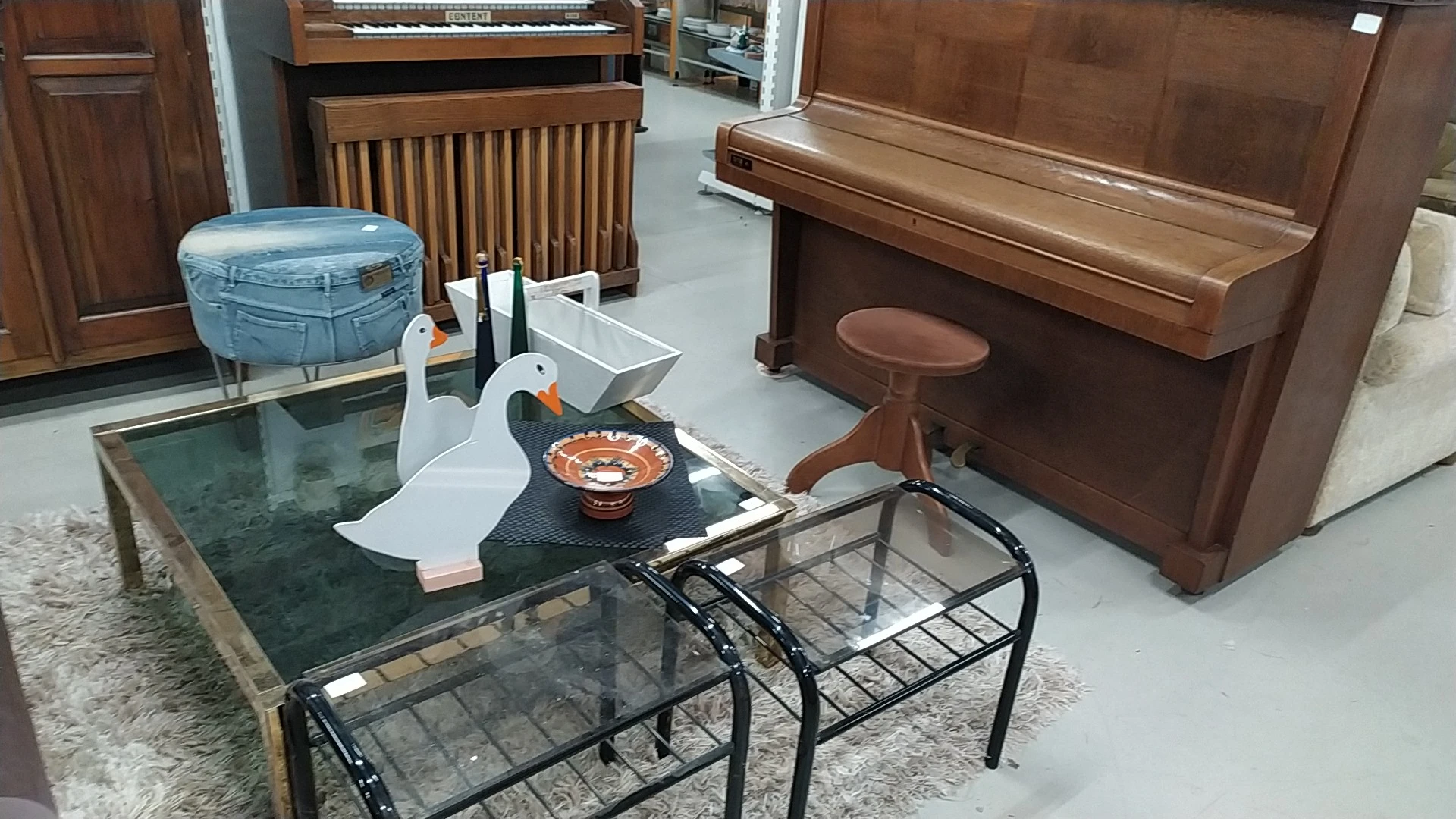 Showroom met meubelen: piano's, orgel, houten radiator, glazen tafels en decoratieve items