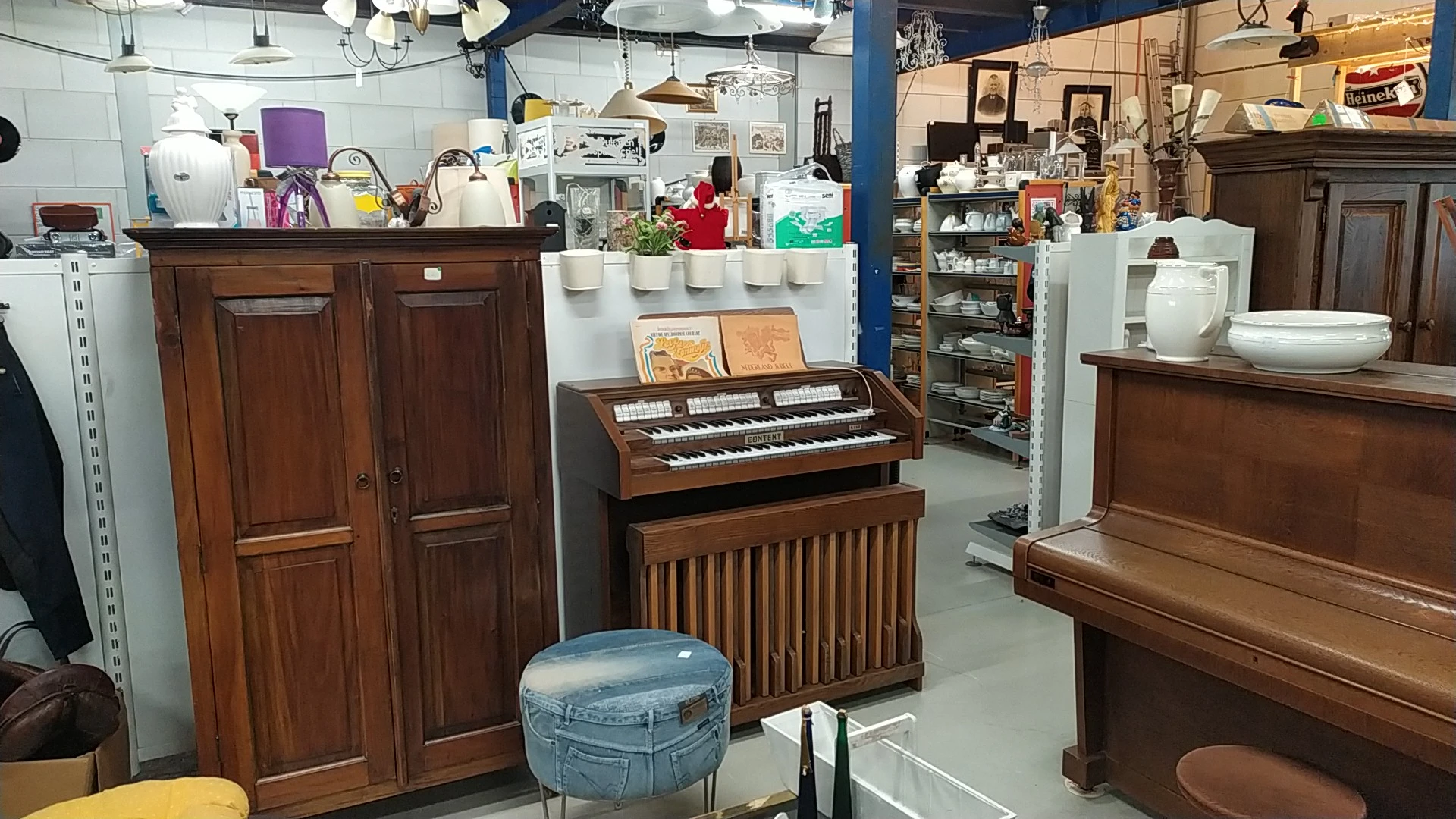 Winkelvloer met houten meubels, een elektronisch orgel, kasten en diverse spullen op stellingen