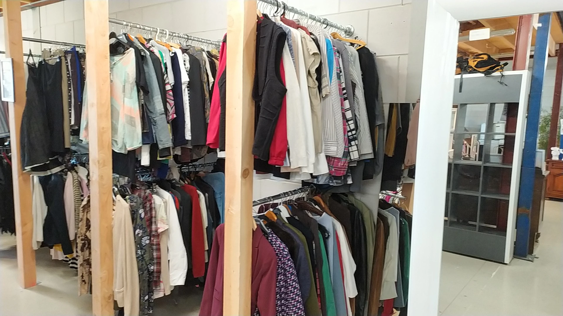 Houten stellingen met uitgestalde tweedehands kleding in verschillende kleuren en stijlen