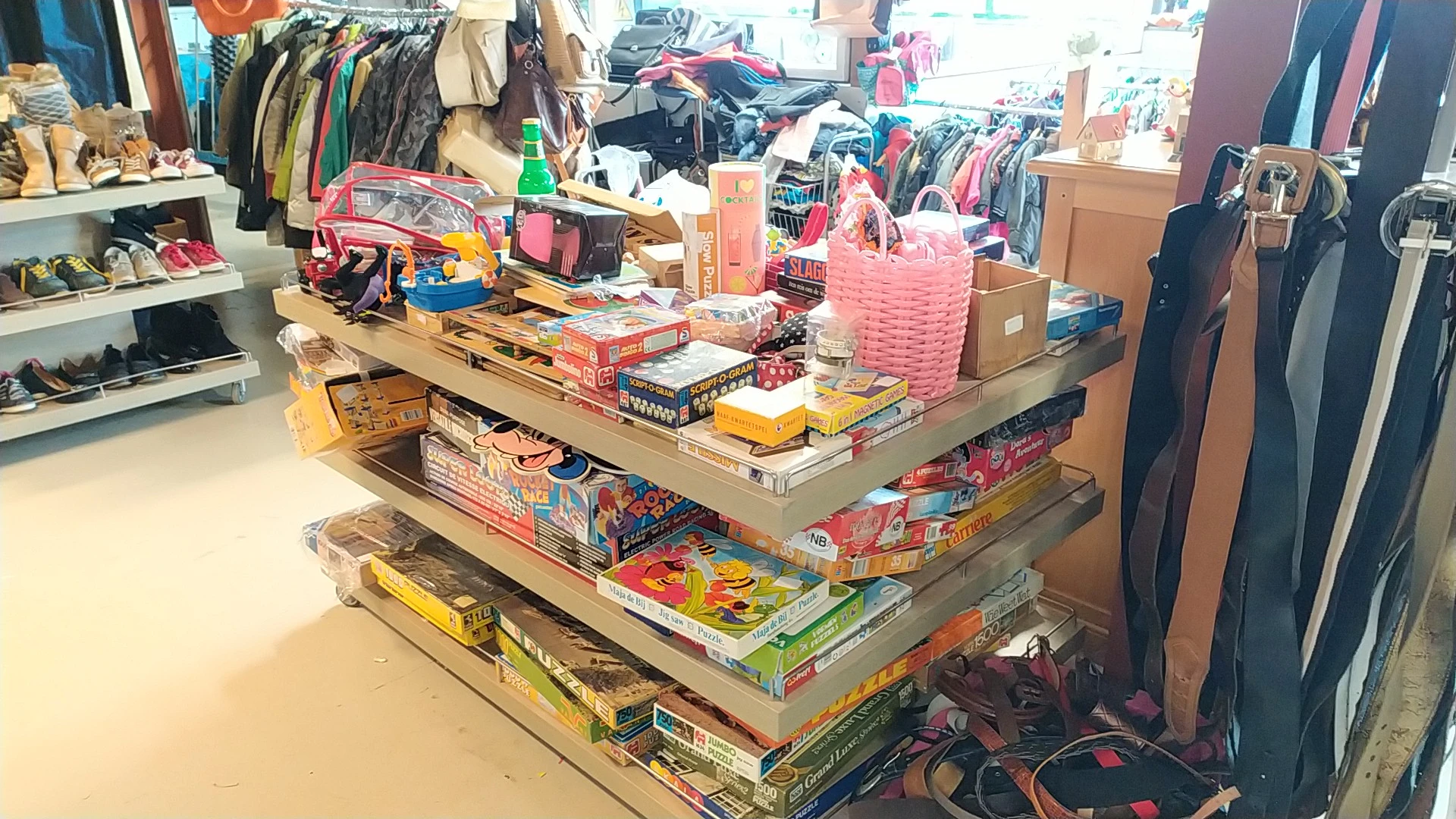 Stapelplateau met speelgoed, bordspellen en kinderartikelen, omgeven door kleding en andere tweedehands goederen