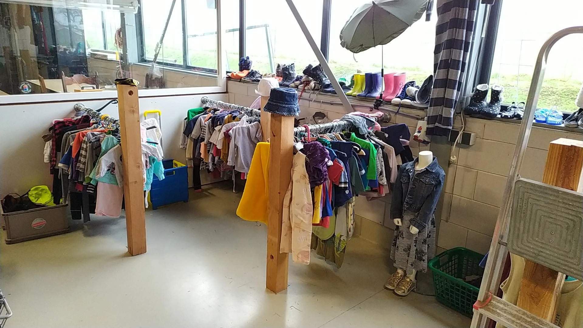 Rekken en hangers vol met tweedehands kleding in verschillende kleuren in een kringloopwinkel