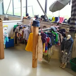 Rekken en hangers vol met tweedehands kleding in verschillende kleuren in een kringloopwinkel