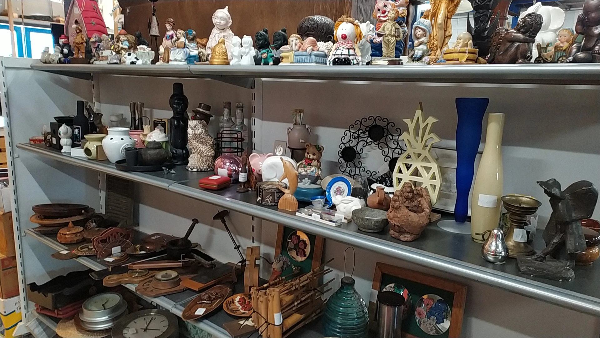 Planken met diverse tweedehands decoratieartikelen, beeldjes, vazen, kandelaren en huishoudspullen