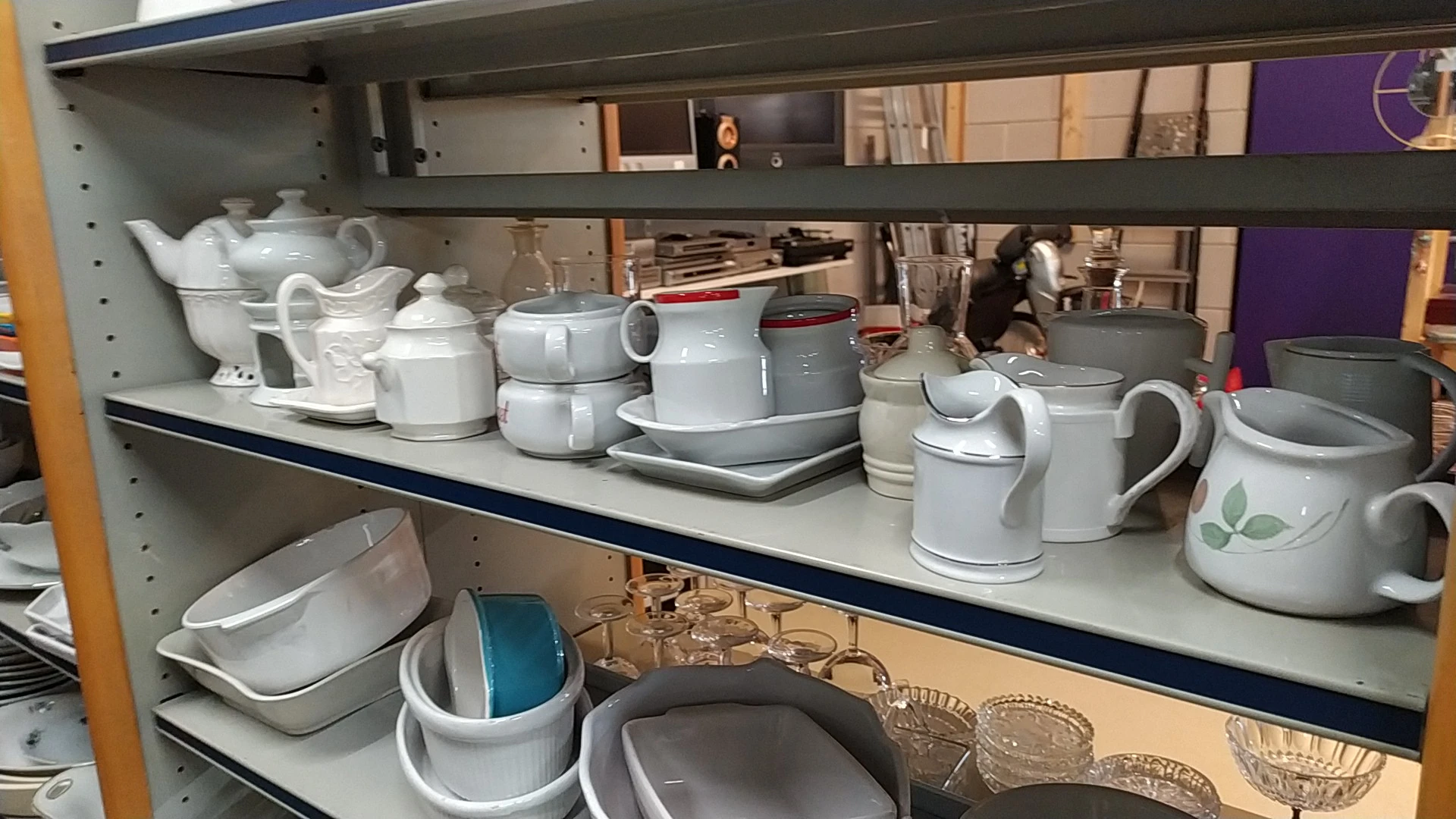 Stellingen met wit serviesgoed, kannen, kopjes en huishoudartikelen in kringloopwinkel
