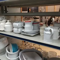 Stellingen met wit serviesgoed, kannen, kopjes en huishoudartikelen in kringloopwinkel
