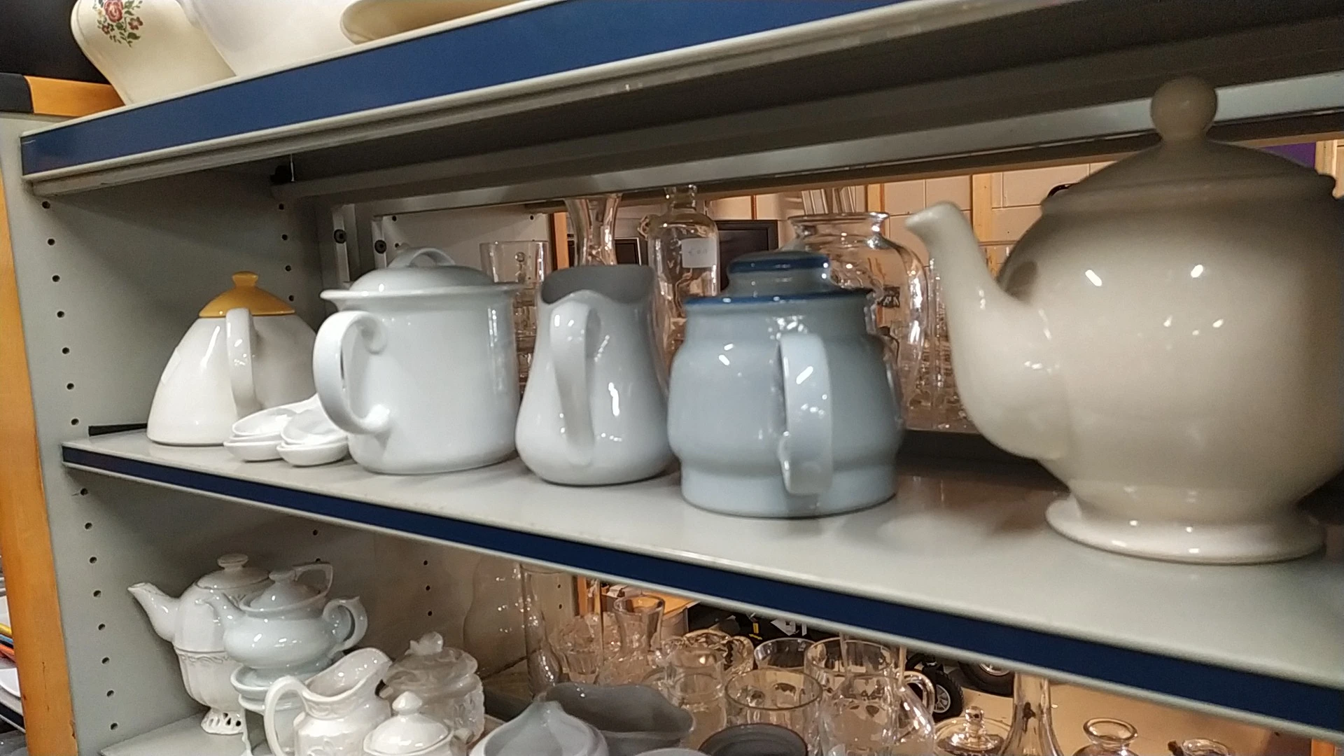 Stellingkast met serviesgoed: witte en grijsblauwe kannen, theepotten en glazen