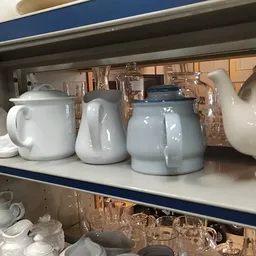 Stellingkast met serviesgoed: witte en grijsblauwe kannen, theepotten en glazen