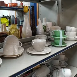 Stellage met serviesgoed: witte kopjes, schotels en groene mokken netjes uitgestald