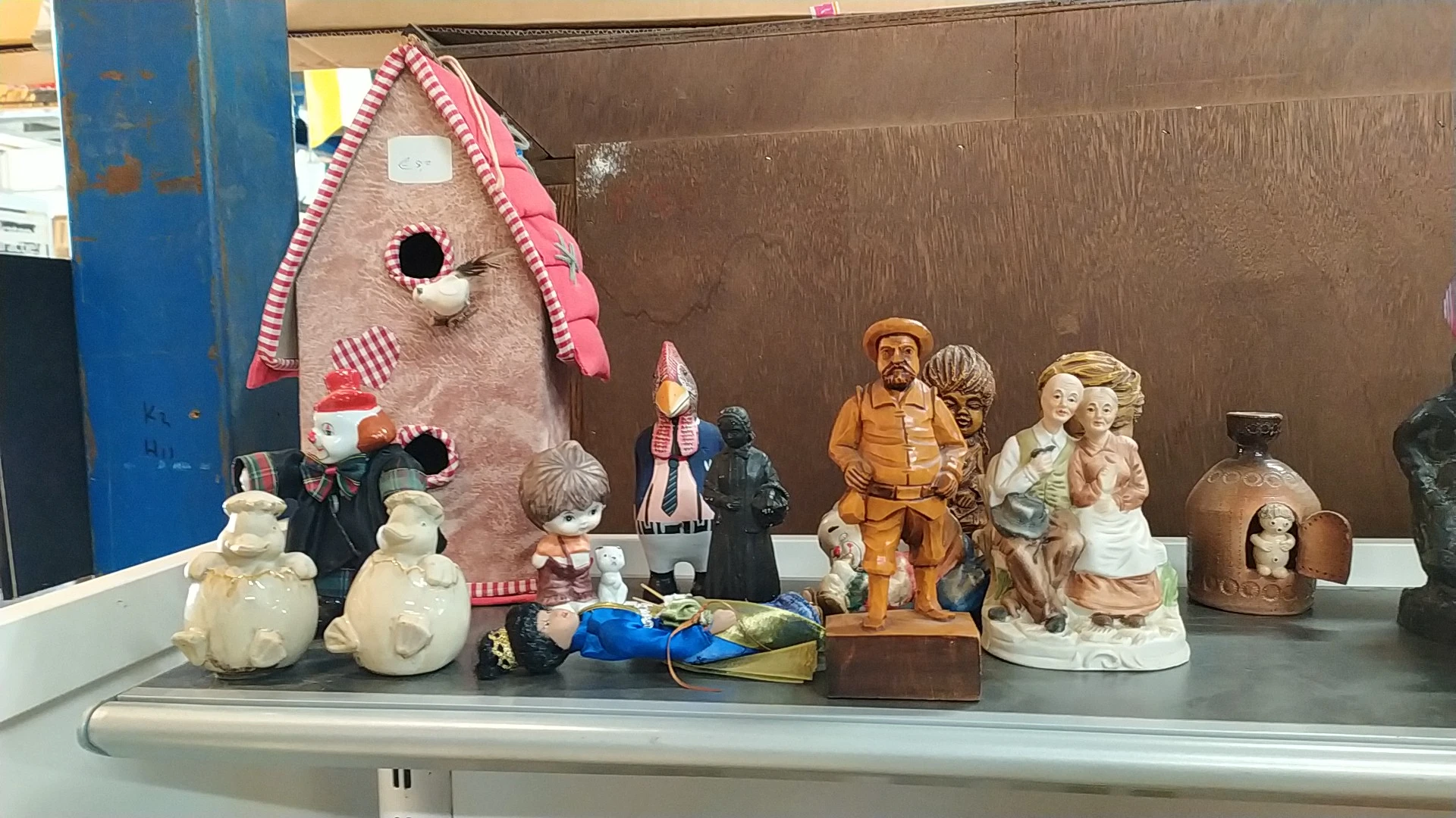 Verschillende vintage en tweedehands decoratieobjecten op een plank: een roze poppenhuis, beelden, vazen en keramische figure