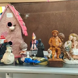 Verschillende vintage en tweedehands decoratieobjecten op een plank: een roze poppenhuis, beelden, vazen en keramische figure