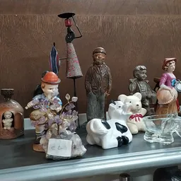 Verzameling tweedehands decoratieartikelen en beeldjes op een tafel: porseleinpoppen, keramische dieren, vintage figuren en o